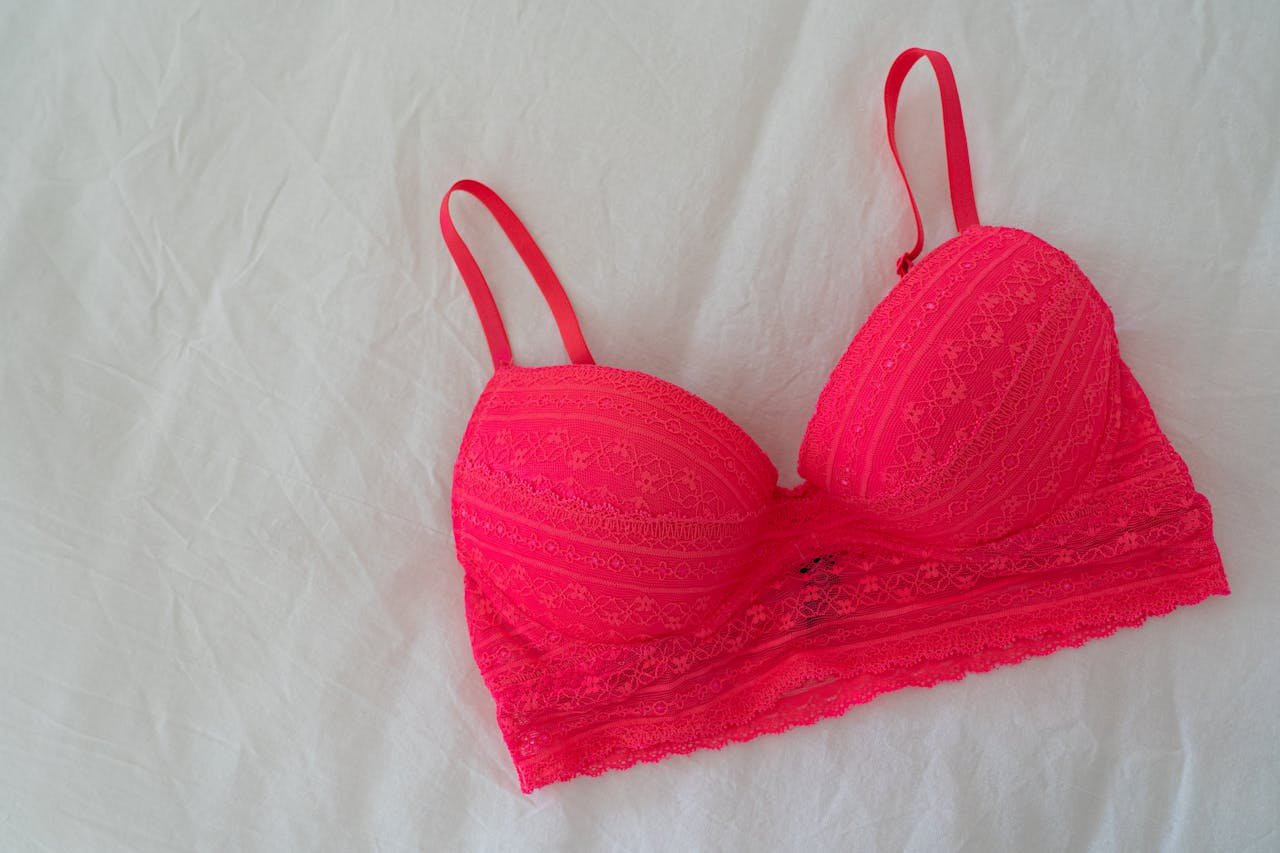 Bright lace pink bra laid flat on soft white sheet.